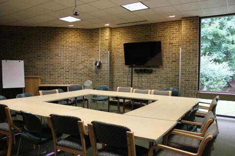 Tables and chairs arranged in Enclosed Square style, with TV screen mounted on wall.