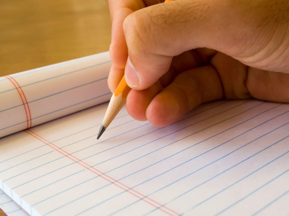 An image of a hand holding a yellow pencil above a pad of lined paper.